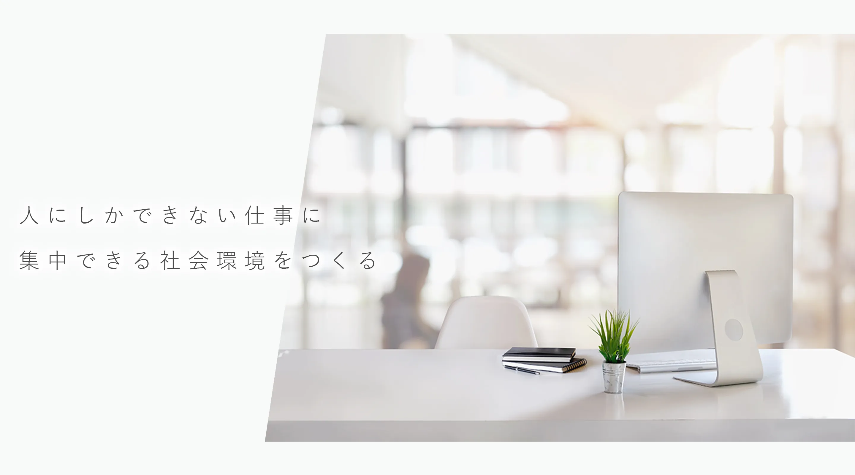 モニターと小さな植物が置かれた明るいデスクの写真