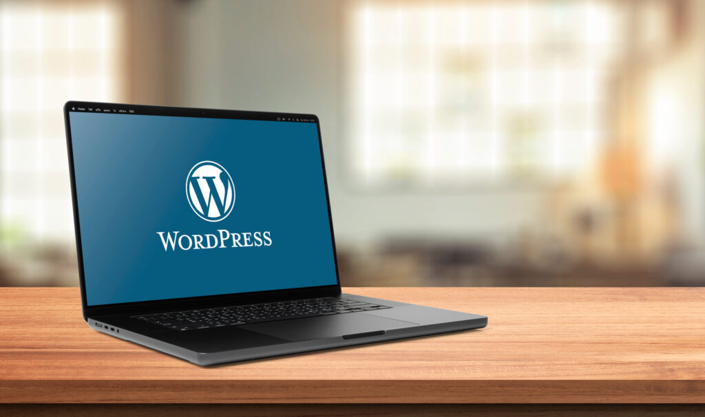 木製のデスク上に置かれたノートパソコンの画面に、WordPressのロゴと文字が表示されている
