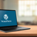 木製のデスク上に置かれたノートパソコンの画面に、WordPressのロゴと文字が表示されている